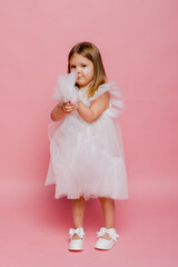 Fototapeta premium A little girl in a white fancy dress on a pink background in the studio
