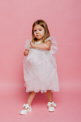 A little girl in a white fancy dress on a pink background in the studio