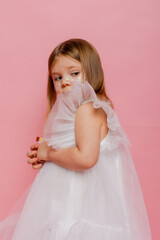 A little girl in a white fancy dress on a pink background in the studio