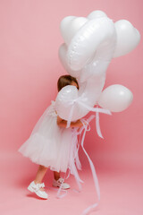 Fototapeta premium little girl with balloons and the number three on a pink background celebrates her birthday in the studio