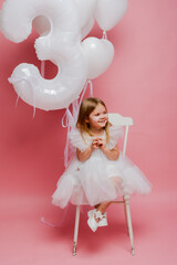 little girl with balloons and the number three on a pink background celebrates her birthday in the studio