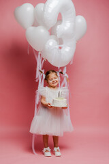 little girl with balloons and the number three on a pink background celebrates her birthday in the studio