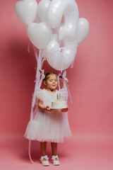 Fototapeta premium little girl with balloons and the number three on a pink background celebrates her birthday in the studio