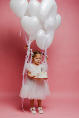 little girl with balloons and the number three on a pink background celebrates her birthday in the studio