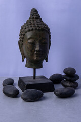 Buddha head sculpture displayed with smooth stones on a light background in a serene arrangement