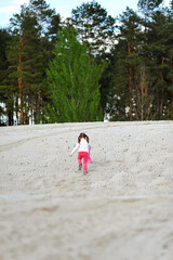 Kid girl with two ponytails running with shovel in her hand on the sand on nature background in the spring. Happy childhood, space for text