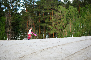 Horizontal shot of happy child girl playing and running with shovel in her hand on the sand on nature background in the spring. Happy childhood