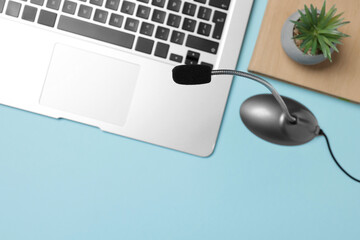 Professional microphone, laptop, notebook and floral decor on light blue background, flat lay