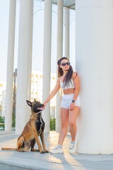 The dog Malinois and the girl in white stand at the column