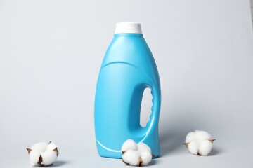 Bottle of fabric softener and cotton flowers on light grey background
