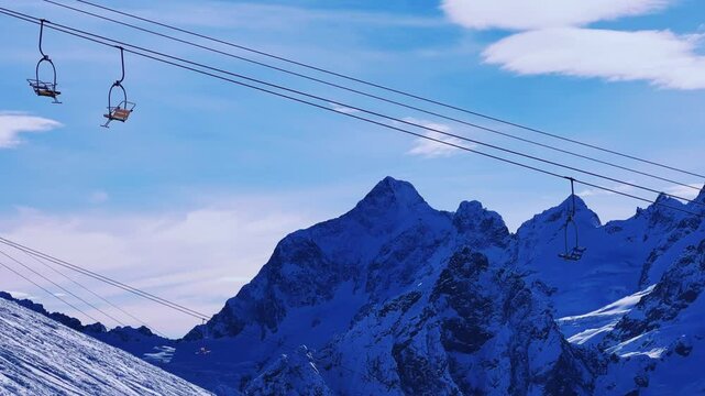 View of the cable car against the backdrop of Dombay glaciers and mountain peaks in the rays of the winter sun.Panorama of the snow-covered Caucasus Mountains in sunny weather. Ski resort in Russia.4К