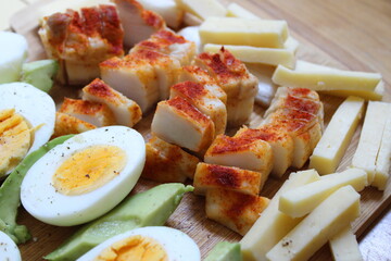 Boiled eggs, sliced cheese, sliced avocado and smoked pork meat on a wooden board