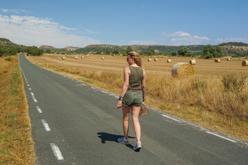 Obraz premium Woman walking along a road with bales of pressed straw in the background