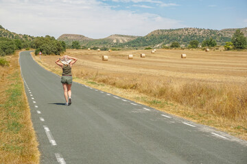 Obraz premium Woman walking along a road with bales of pressed straw in the background