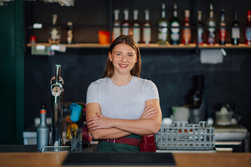 Smiling barista posing with crossed arms in modern cafe