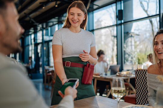 Waitress holding pos terminal accepting contactless payment from customer in restaurant