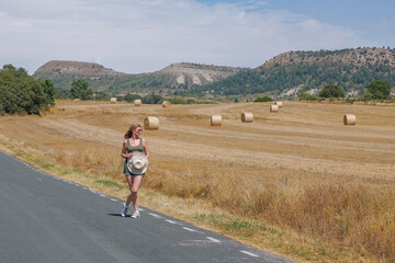 Obraz premium Woman walking along a road with bales of pressed straw in the background