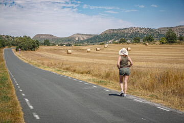 Obraz premium Woman walking along a road with bales of pressed straw in the background