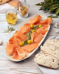 ham sliced ​​and laid out on a white plate, bread, greens, and olive oil on a wooden table