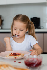Two little girls are having breakfast at home in the kitchen with waffles and jam