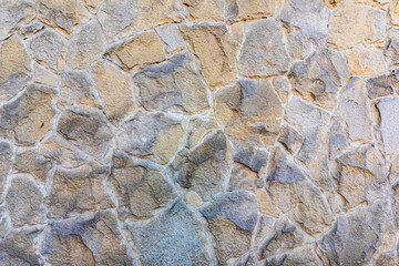 Close-up of a wall made from natural, irregularly shaped beige and gray stones with visible mortar joints.