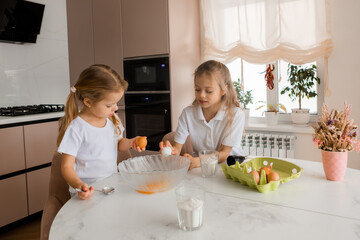 Two little girls cook cookies at home in the kitchen