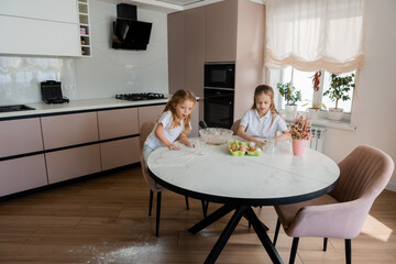 Two little girls cook cookies at home in the kitchen