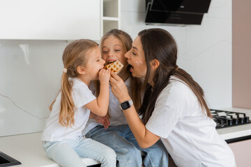 mom and two daughters in the kitchen eating cookies