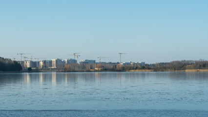 Naklejka premium A modern residential area by a water body in the city, showcasing new home construction and the demolition of older structures. The urban landscape reflects the transition of winter into spring.