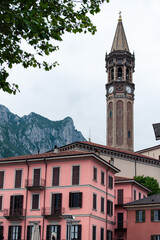 View over Lecco's traditional rooftops and the historic San Nicolò campanile, Lombardy, Italy. Classic Italian architecture set against a backdrop of the misty Prealpine mountains
