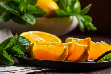Oranges, lemons, limes, mint and lemon balm and raindrops illuminated by the sun on a wooden background.