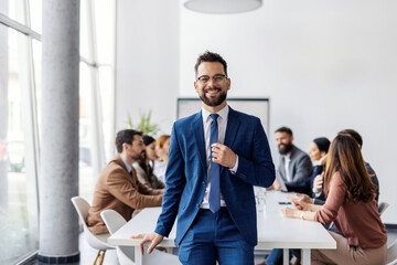 Portrait of manager sitting at conference table with her leadership team and smiling at camera during meeting.