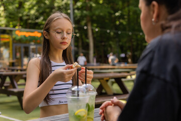 teenage girl drinks a cocktail and eats pizza in the summer at a cafe on the street