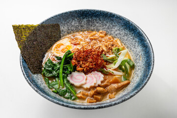 Spicy miso ramen with noodles, seaweed, spinach, egg, chili, narutomaki, and green onions in a rustic blue bowl on a white background.