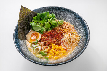 Vegetarian miso ramen with noodles, seaweed, greens, corn, egg, and chili in a rustic blue bowl on a white background. A vibrant, traditional Asian dish showcasing Chinese and Japanese culinary styles