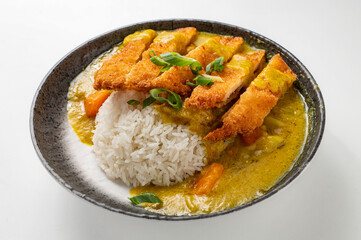 Chicken katsu curry rice with crispy breaded chicken, creamy curry sauce, carrots, and sticky rice, garnished with green onions in a rustic black bowl on a white background