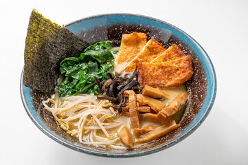 Vegetarian miso ramen with noodles, seaweed, spinach, mushrooms, bean sprouts, and tofu in a rustic blue bowl on a white background
