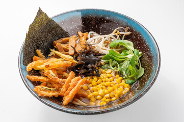 Vegetarian shoyu ramen with noodles, seaweed, corn, greens, mushrooms, and tempura in a rustic blue...