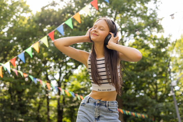 Happy teenage girl listens to music with headphones in summer park
