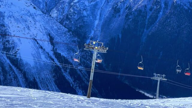 View of the cable car against the backdrop of Dombay glaciers and mountain peaks in the rays of the winter sun.Panorama of the snow-covered Caucasus Mountains in sunny weather. Ski resort in Russia.4К