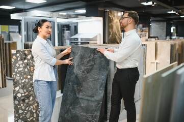 Fototapeta premium Shop assistant showing ceramic tile to woman in hardware store