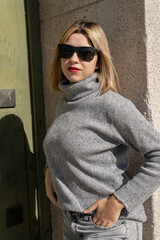 Blonde woman wearing sunglasses and turtleneck sweater posing near green door