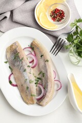 Tasty herring fillets with onions and parsley served on white table, flat lay