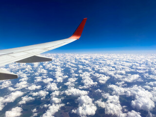 View from airplane window to airplane wing, and clouds from above the sky.