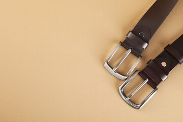 Two leather belts on beige background, flat lay. Space for text