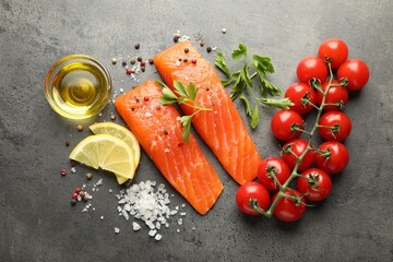 Seafood. Pieces of salmon fillet, tomatoes, lemon slices, oil and spices on gray textured table, flat lay