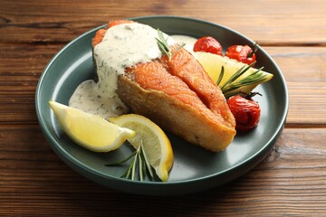 Seafood. Tasty salmon steak served with sauce, tomatoes, rosemary and lemon on wooden table, closeup
