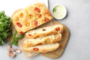 Cut delicious focaccia with tomatoes, spices and oil on gray table, flat lay