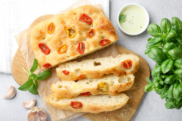 Cut delicious focaccia with tomatoes, spices and oil on gray table, flat lay
