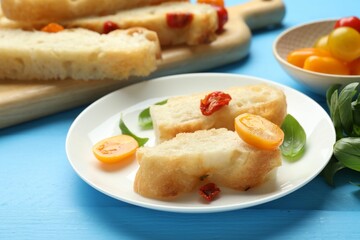 Pieces of delicious focaccia with tomatoes and basil on light blue wooden table, closeup